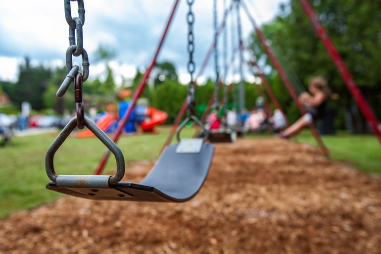 swing set in a playground with children playing in the background