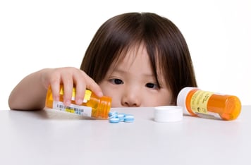 A young girl looks at a pile of pills that was left on a counter.