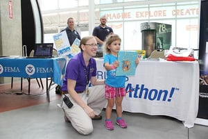 Kansas City, Mo. -- Science City Educator Heather Edvenson, gives Anna Thompson of Leavenworth, Kan., a book, as a prize for participating in their Shakeout earthquake drill at Science City (inside Union Station), Sat., Aug. 22, 2015. The drill was part of an America's PrepareAthon event. FEMA photo Amanda Bicknell