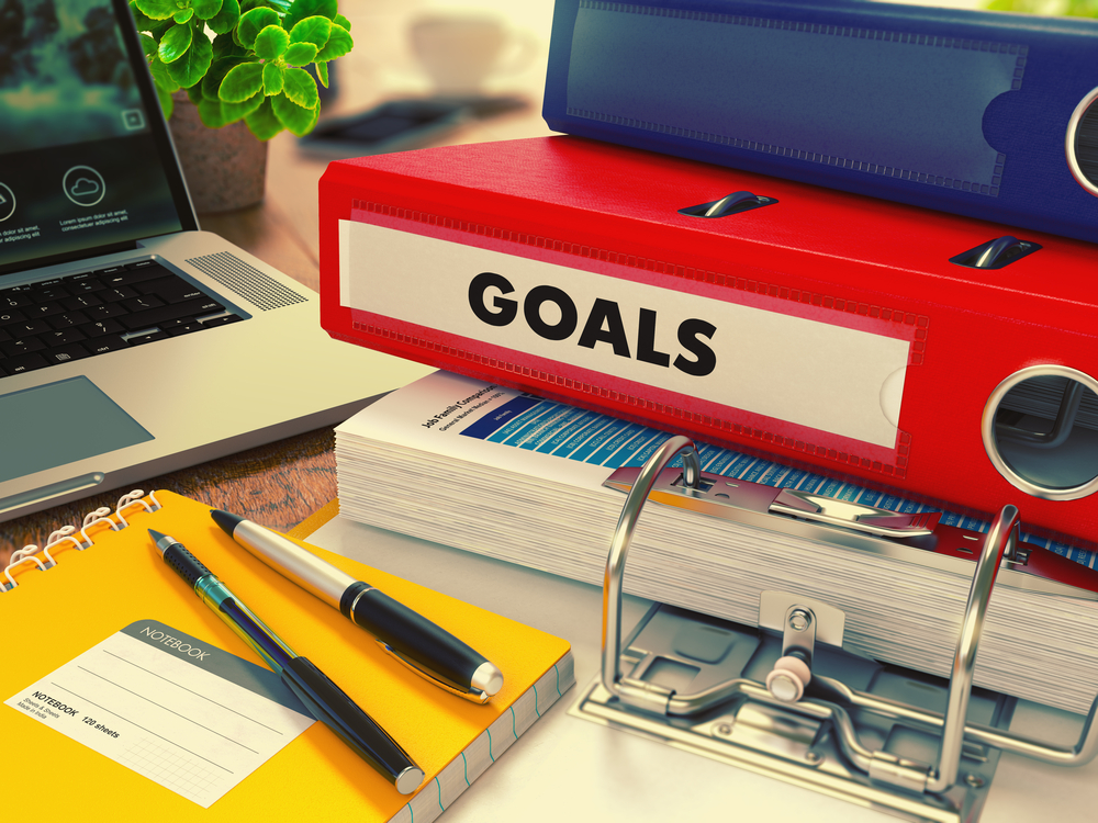 Red Office Folder with Inscription Goals on Office Desktop with Office Supplies and Modern Laptop