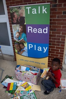 A child sits next to Talk, Read, Play collection box.